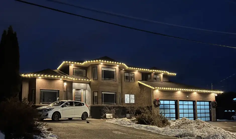 A two-storey home with warm white Christmas lights fitted evenly along the roofline and garage at night.