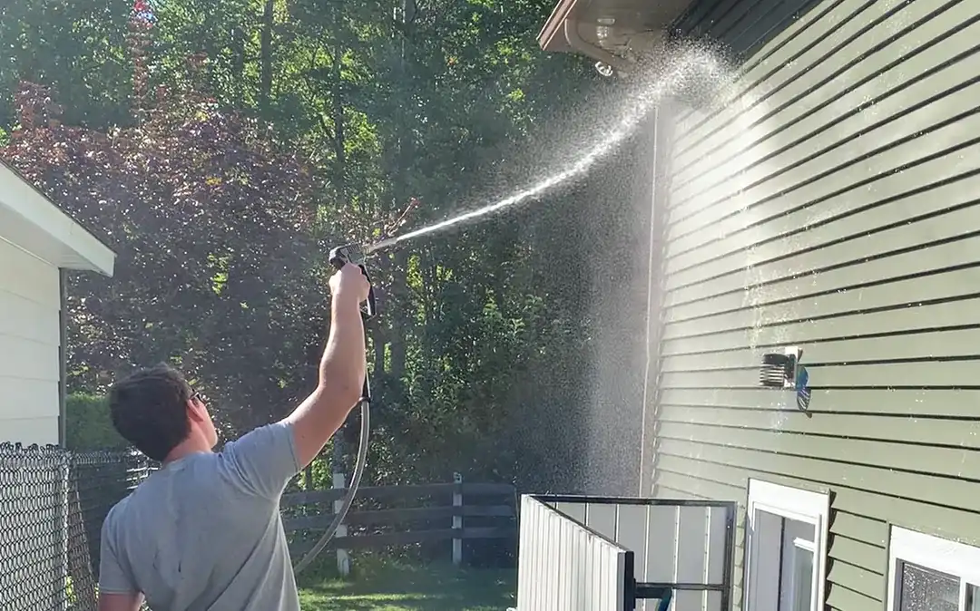 A Shine technician rinsing the upper courses and soffit of a two-storey home from the ground with a low-pressure spray.