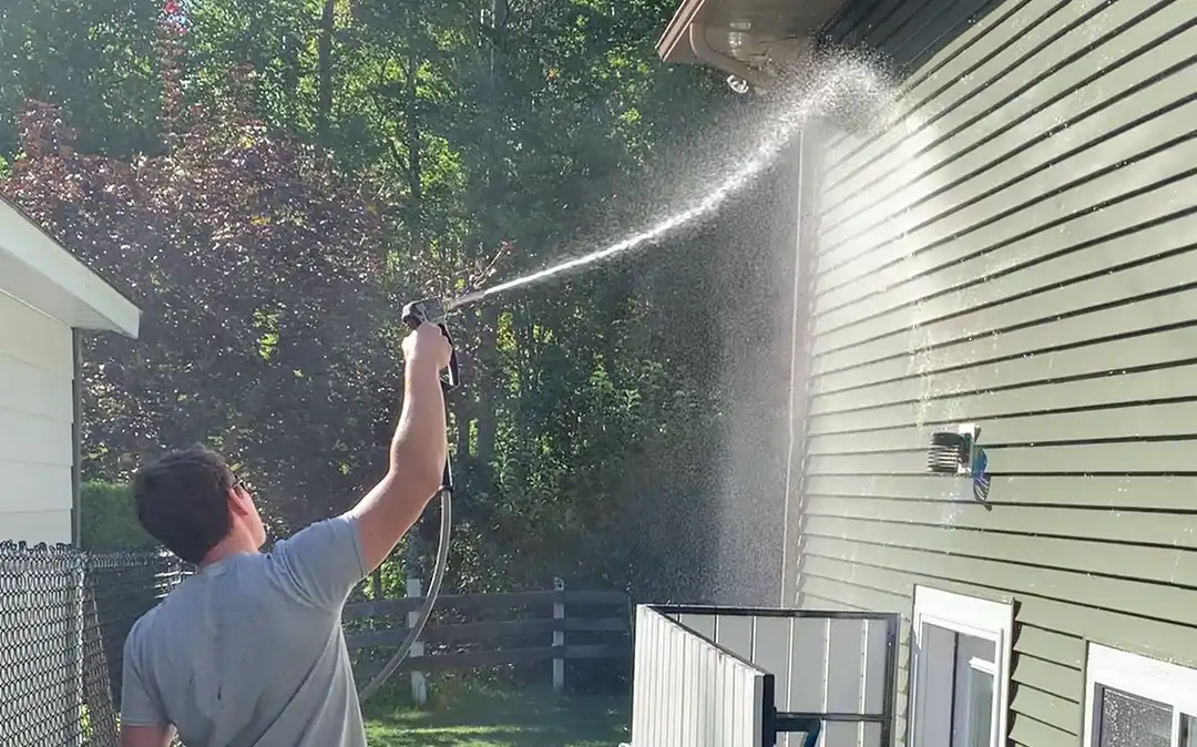 A Shine technician rinsing the upper courses and soffit of a two-storey home from the ground with a low-pressure spray.