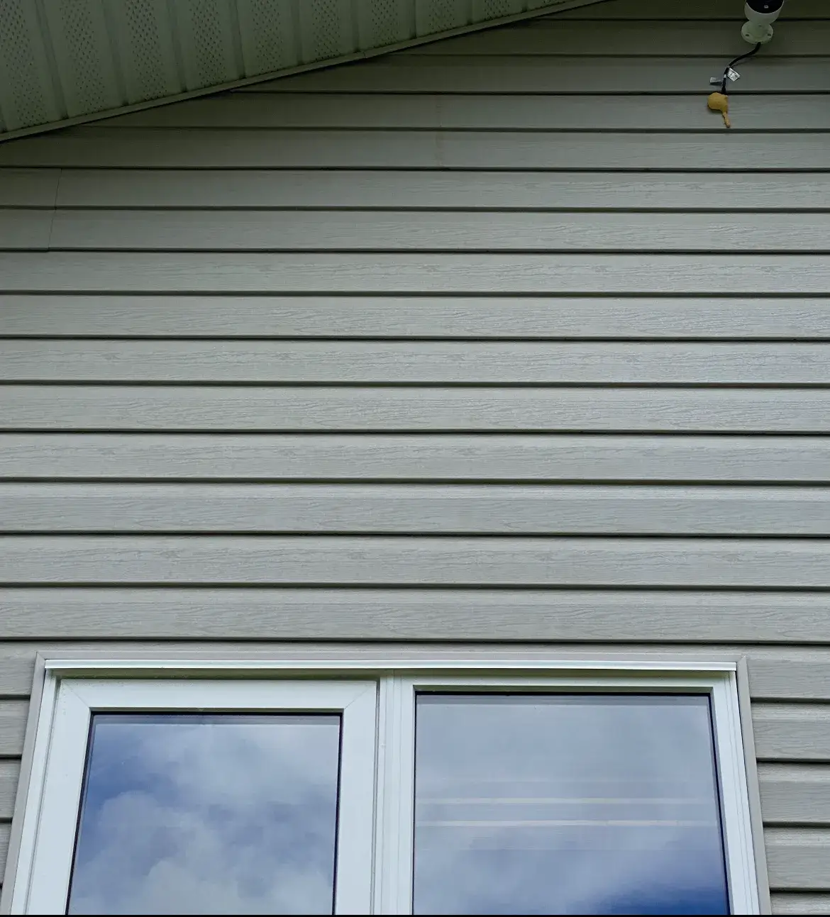 The same sage-green vinyl siding and soffit after soft washing, the horizontal streaking gone and the colour even across every course.