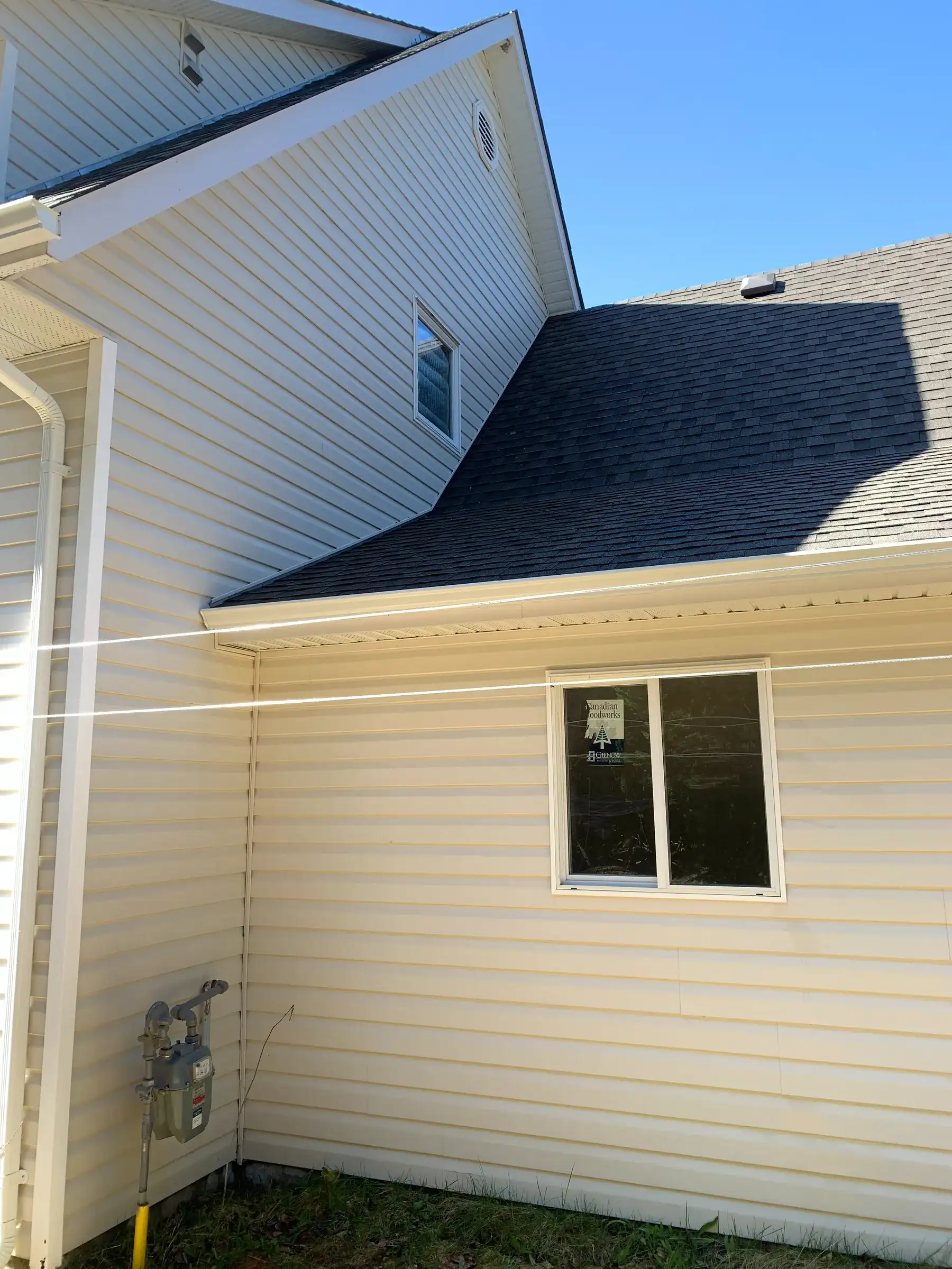 The same two-storey house after soft washing, the siding clean and even, the same gable window and gas meter in frame under a clear sky.