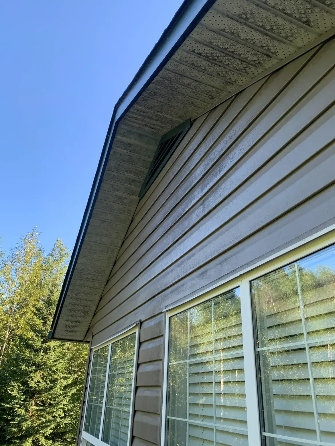 A vented soffit and the siding beneath it darkened with green algae and grime, a gable vent set into the wall.