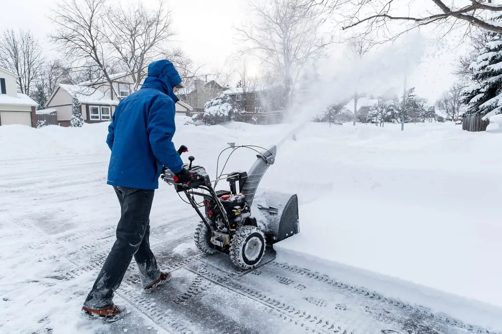 A person using a snowblower to clear deep snow from a residential driveway after a heavy snowfall.