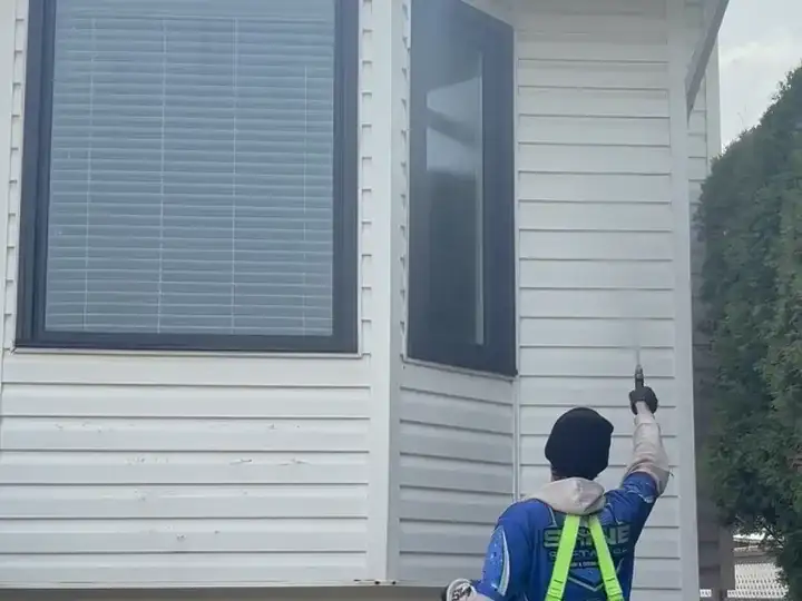 A Shine technician using a water-fed pole to clean second-storey exterior windows while standing on the ground.