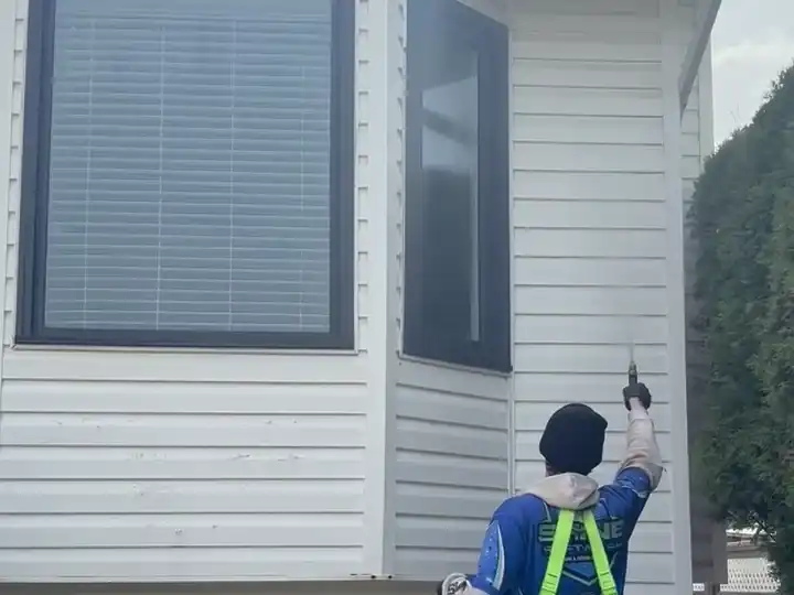 A Shine technician using a water-fed pole to clean second-storey exterior windows while standing on the ground.