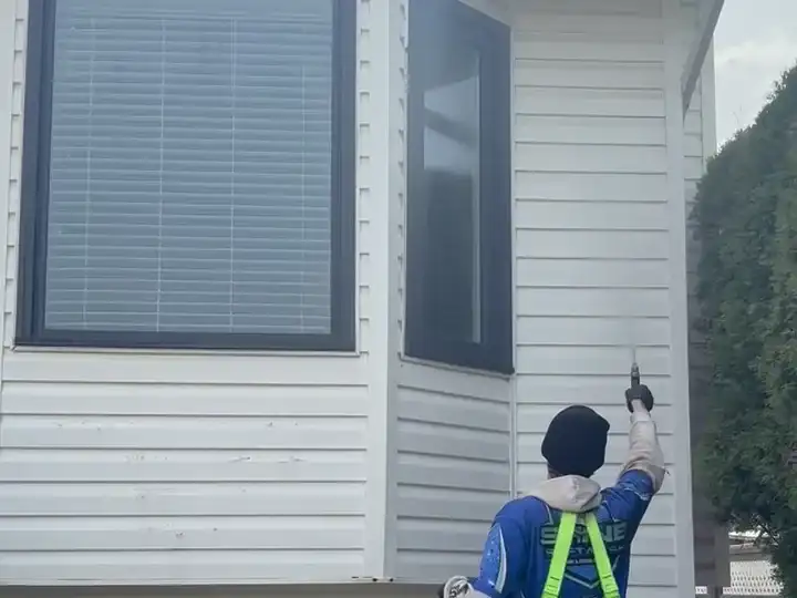 A Shine technician using a water-fed pole to clean second-storey exterior windows while standing on the ground.